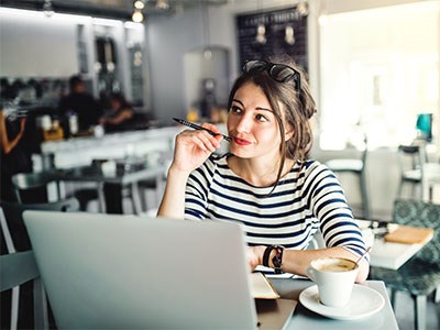 Woman at laptop at coffee shop thinking of ideas.