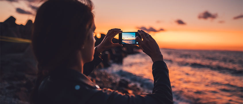 Photo of woman taking landscape photo of beach at sunset. 