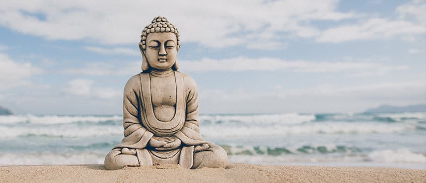 Buddha stone figure sitting on the seashore in front of the slightly rough sea