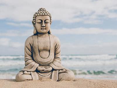 Buddha stone figure sitting on the seashore in front of the slightly rough sea