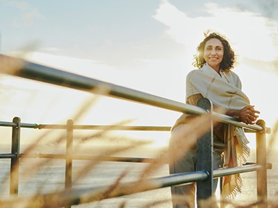 Woman standing on pier by water with a railing creating a boundary between her and the camera.