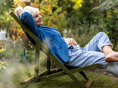 Person relaxing in a reclining chair surrounded by a lush garden, symbolizing stress-free gardening and enjoying nature in a serene outdoor setting.