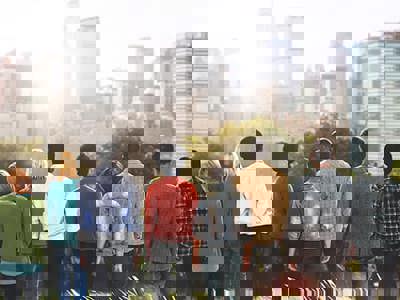 A group of people standing in a line with their backs towards the camera as they look over a city skyline in the sunshine. 