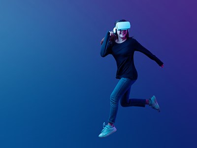 Girl in dark shirt, jeans and tennis shoes running in an empty blue-coloured, virtual space and wearing a VR headset.