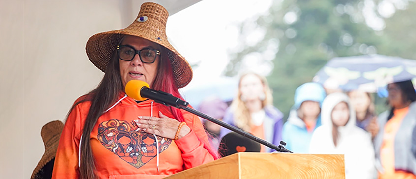 Robina Thomas speaks at a podium during the Orange Shirt Day event in 2025 at the University of Victoria.