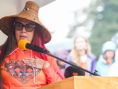 Robina Thomas speaks at a podium during the Orange Shirt Day event in 2025 at the University of Victoria.