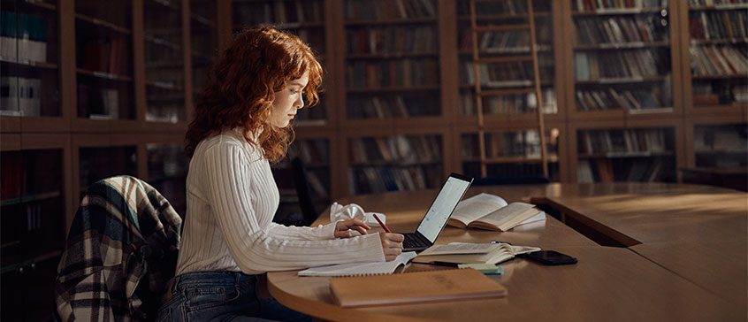 A female student taking notes and looking at a laptop.