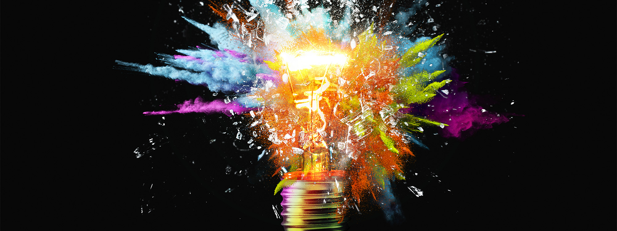 Creative light bulb explodes with colourful paint splashes on a black background.