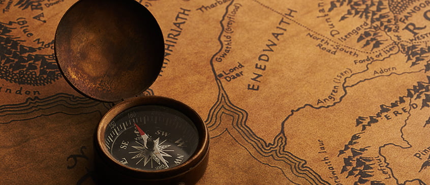 Vintage compass resting on a detailed fantasy map with intricate place names and terrain, symbolizing imaginative cartography and creative world-building.