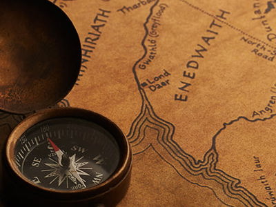 Vintage compass resting on a detailed fantasy map with intricate place names and terrain, symbolizing imaginative cartography and creative world-building.
