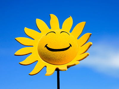 A happy face sunflower with a bright blue sky in the background.