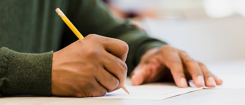 Close-up of hands writing with a yellow pencil on paper, representing French language examination preparation and testing