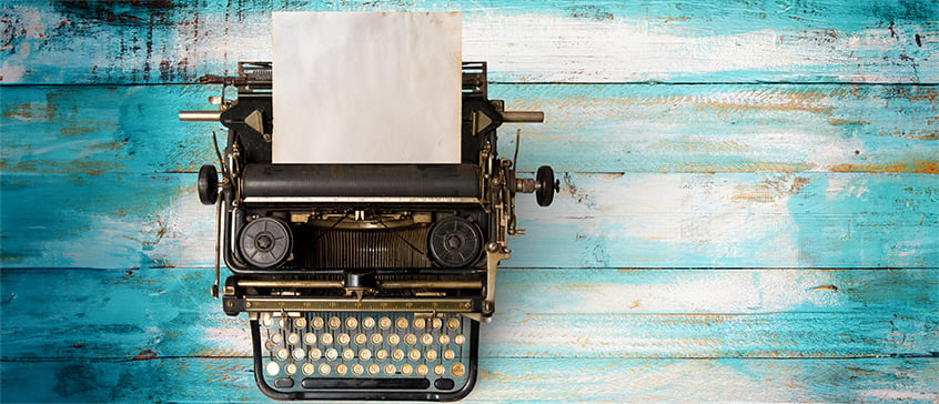 Top view of a vintage typewriter with old paper sitting on a faded blue table top.