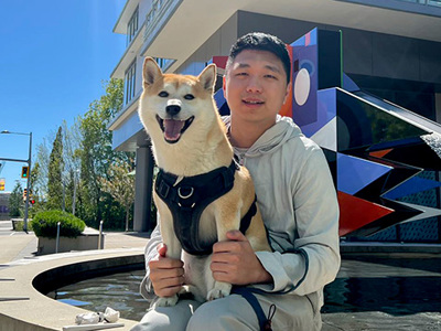 On a sunny day, Yanqing sitting with his dog outside on a fountain near UVic