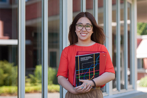 Photo of UVic student holding workbooks and smiling at the camera.