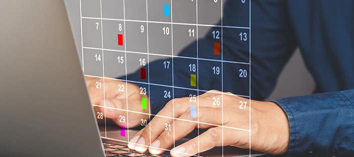 Hands typing on a laptop keyboard with a transparent calendar showing marked days flagged.