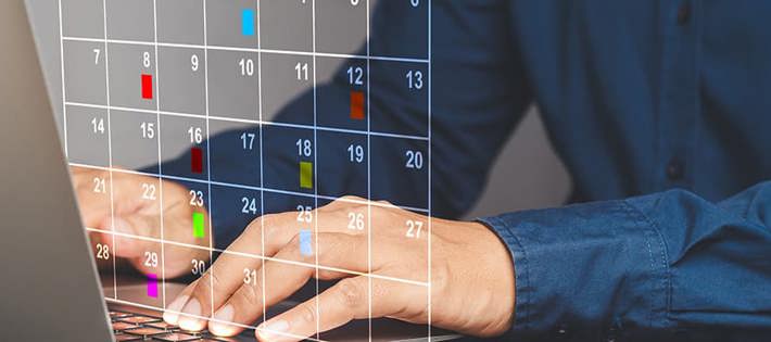 Hands typing on a laptop keyboard with a transparent calendar showing marked days flagged.