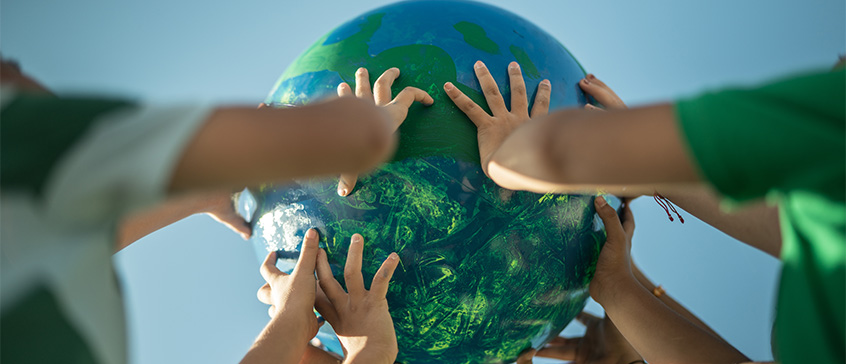 A group of diverse hands reaching up to hold a globe against a clear blue sky.