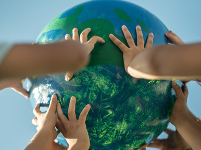A group of diverse hands reaching up to hold a globe against a clear blue sky.