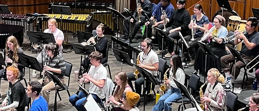 UVic concert band in rehearsal. A long shot of musicians in an orchestra formation playing various wind instruments.