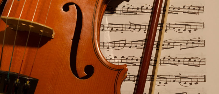 Close-up of violin and bow resting on classical sheet music, evoking the timeless tradition of traveling to experience iconic classical music performances in renowned venues worldwide