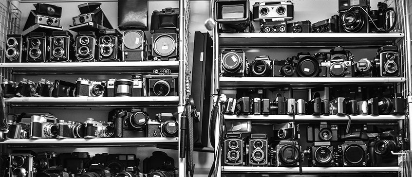 Photo of vintage cameras stacked on a shelf. 