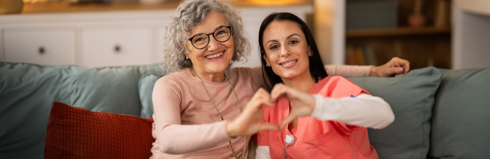 Two smiling women making a heart shape with their hands.