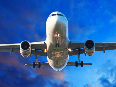 View from below as a passenger plane coming in for a landing.  Plane is in flight with a landing gear down. Twilight blue with clouds in the sky behind it. 