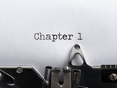 Close-up of a vintage typewriter with white paper inserted, showing Chapter 1 typed at the top of the page, representing the beginning of the novel writing process.