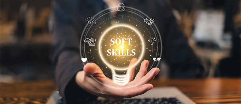  An abstract image showing a hand holding a glowing lightbulb with "SOFT SKILLS" written inside, surrounded by a circle of icons representing various skills like communication, empathy, and problem-solving.