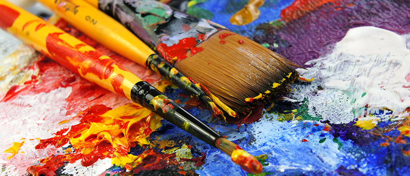Closeup photo of paintbrushes on top of paint splotches. 