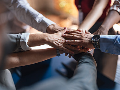Multiple hands of diverse individuals coming together in a team huddle or group handshake, symbolizing collaboration, unity, and collective support in workforce development and lifelong learning initiatives.