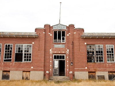 Abandoned red-brick school building with broken windows and boarded doors, representing a former residential school and the legacy of colonial policies in Canada.