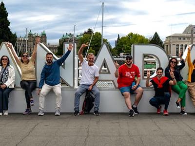 A group of international teachers on a tour of Victoria sitting in front of a sculpture spelling out the word Canada