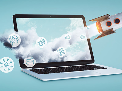 
A white laptop computer is open and facing left on a light blue background. A stream of white clouds billows out from the laptop screen, moving towards the right. Embedded within the clouds are several white line-art icons related to digital marketing. A rocket with an orange nose cone and fins is launching upwards from the right side of the laptop, leaving a trail of smoke and fire. Additionally, two other icons, a megaphone and a speech bubble, are positioned to the lower left of the laptop, outside the cloud stream. This image symbolizes the rapid growth and diverse tools within digital marketing.