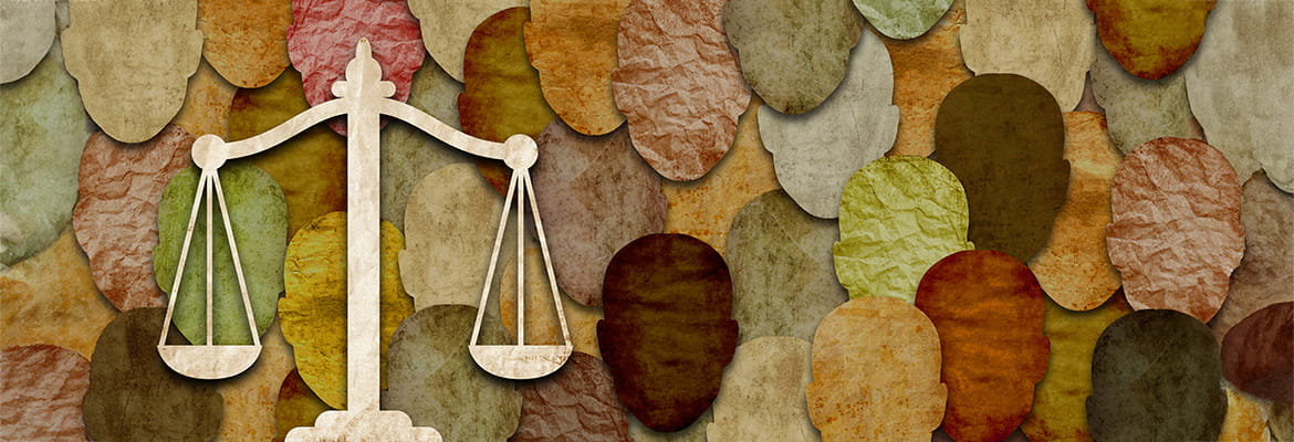 Paper cutouts of multicoloured heads depicting an ethnically diverse population. A marbled scales of justice are overlaid resting in a balanced position symbolizing social justice and equality