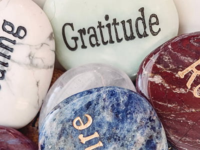 Coloured, polished stone in a pile with words and thoughts engraved on them like Gratitude, Healing and Relax.