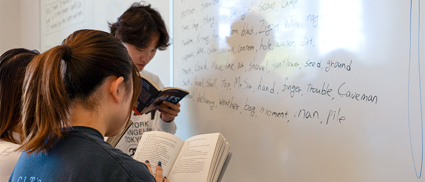 Students looking at books in front of whiteboard