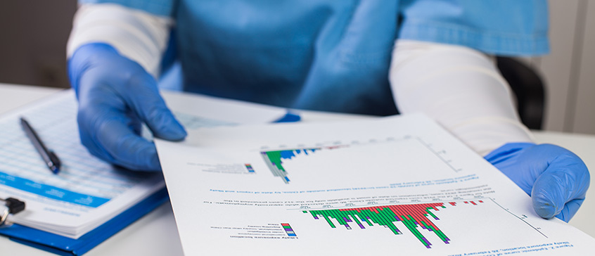 A medical worker holding a paper with graphs. They are in blue scrubs and wearing latex gloves 