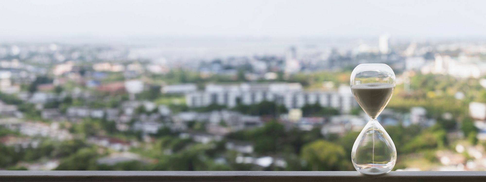 Hourglass on a ledge with a blurred city view in the background.