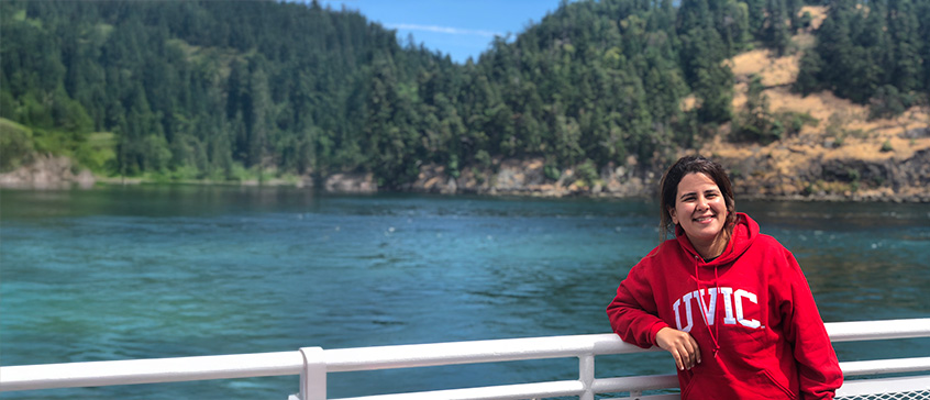 International student in a red UVIC hoodie stands at the railing of a BC Ferry passing through Active Pass.