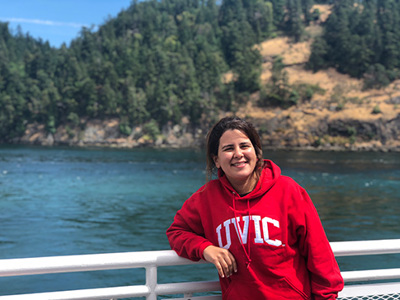 International student in a red UVIC hoodie stands at the railing of a BC Ferry passing through Active Pass.