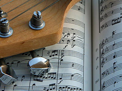 Close-up of a guitar headstock resting on an open sheet of classical music notation, featuring staves, notes, and chords, symbolizing the study of music theory and performance.