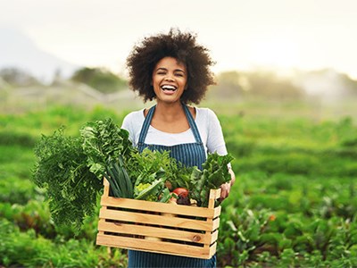 Woman standing in field with a big basket of vegetables. 