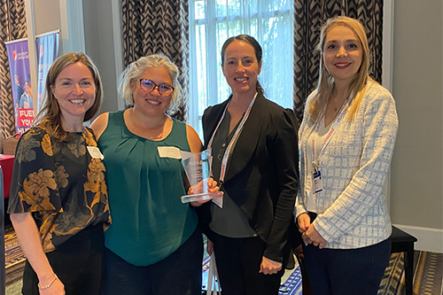 Four women standing together and smiling at the BCCIE International Education Awards. One of them is holding an award.