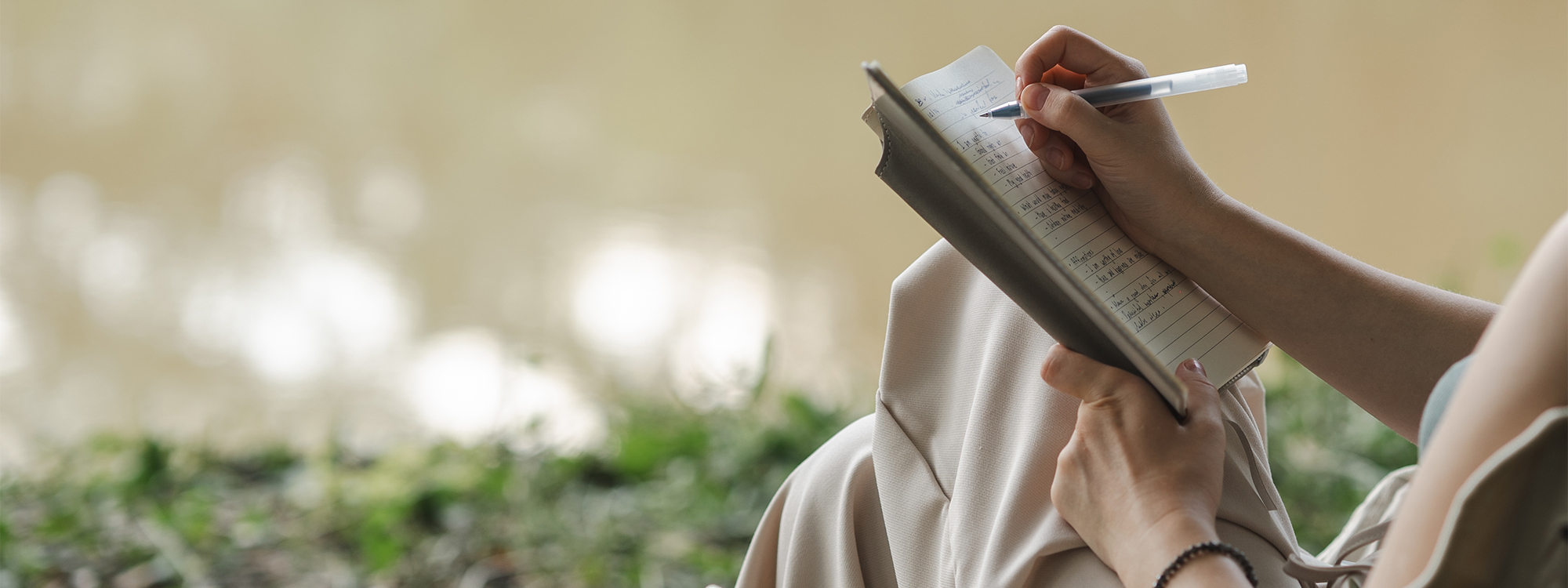Person writing in a journal while sitting in a field,