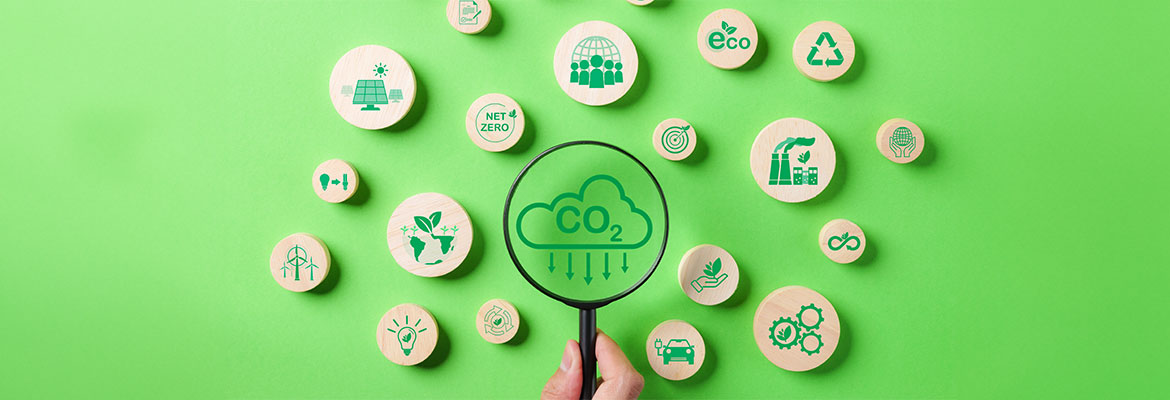A hand holds a magnifying glass over a CO2 icon, surrounded by other eco-friendly icons on a green background.