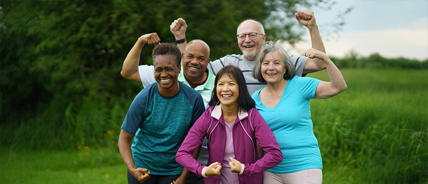 Group of people outdoors in a grassy area flexing their arms in a strong pose, symbolizing health, fitness and community wellness.