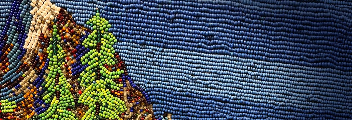 Photo of a beaded scene of trees and mountains on a blue sky.