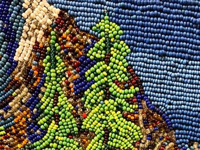 Photo of a beaded scene of trees and mountains on a blue sky.